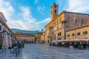 Piazza del Popolo ad Ascoli Piceno al tramonto, meta ideale per un week end in città in Italia, con edifici storici in travertino e caffè all'aperto