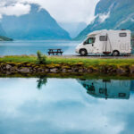 Camper parcheggiato in riva a un lago in autunno, circondato da montagne e paesaggi naturali