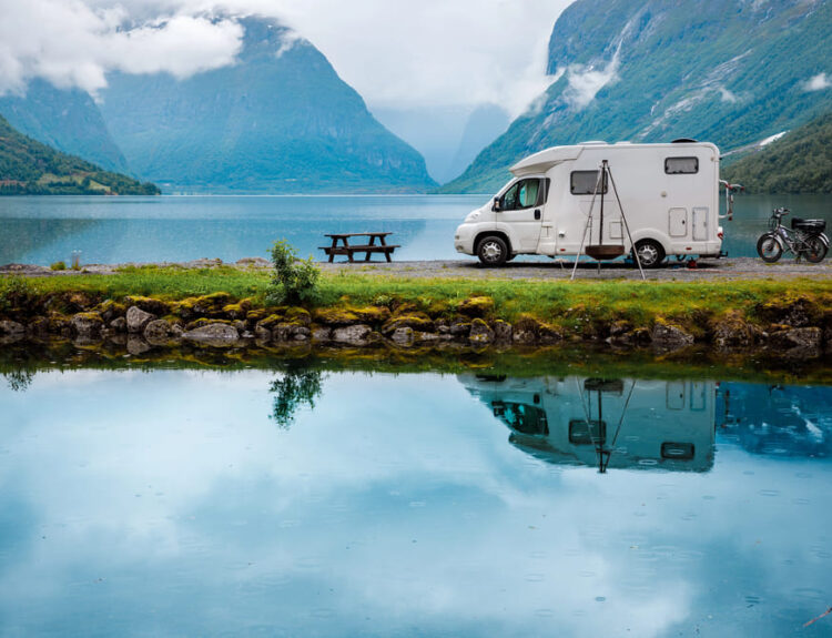 Camper parcheggiato in riva a un lago in autunno, circondato da montagne e paesaggi naturali