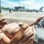 Viaggiatore che dorme in aeroporto con un biglietto in mano, rappresentando il concetto di sleep tourism e relax durante i viaggi