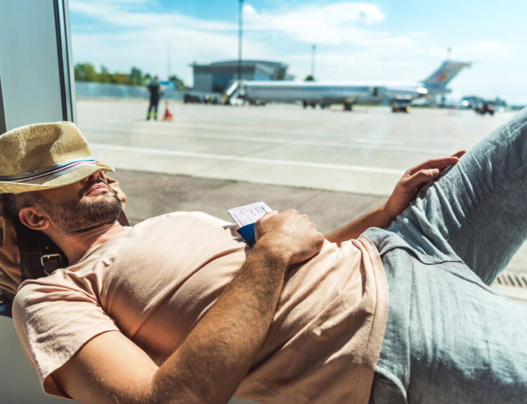 Viaggiatore che dorme in aeroporto con un biglietto in mano, rappresentando il concetto di sleep tourism e relax durante i viaggi