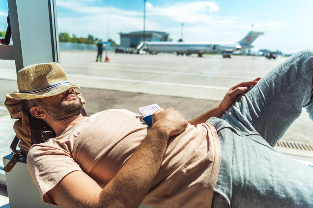 Viaggiatore che dorme in aeroporto con un biglietto in mano, rappresentando il concetto di sleep tourism e relax durante i viaggi